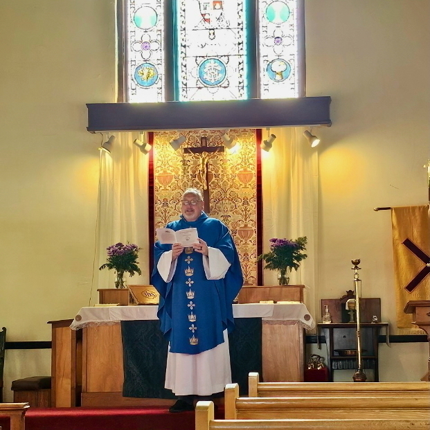 An Anglican Priest stands before an altar decked in blue for Advent